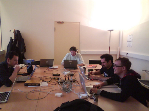 5 men sitting around a table coding on their computers